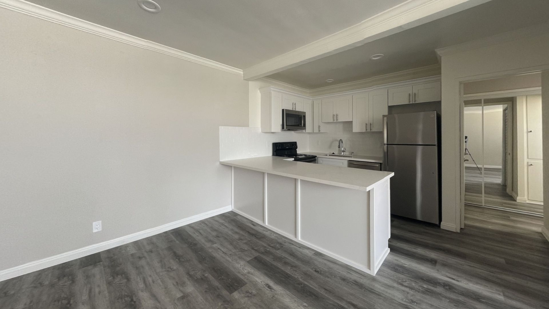 Empty kitchen with white cabinets, stainless steel fridge, and gray flooring.