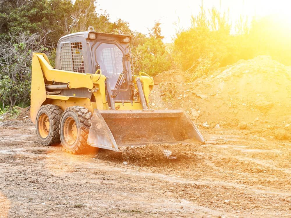 A Yellow Bulldozer Is Driving Down A Dirt Road — Brown's Vegetation Management In Mulara, QLD