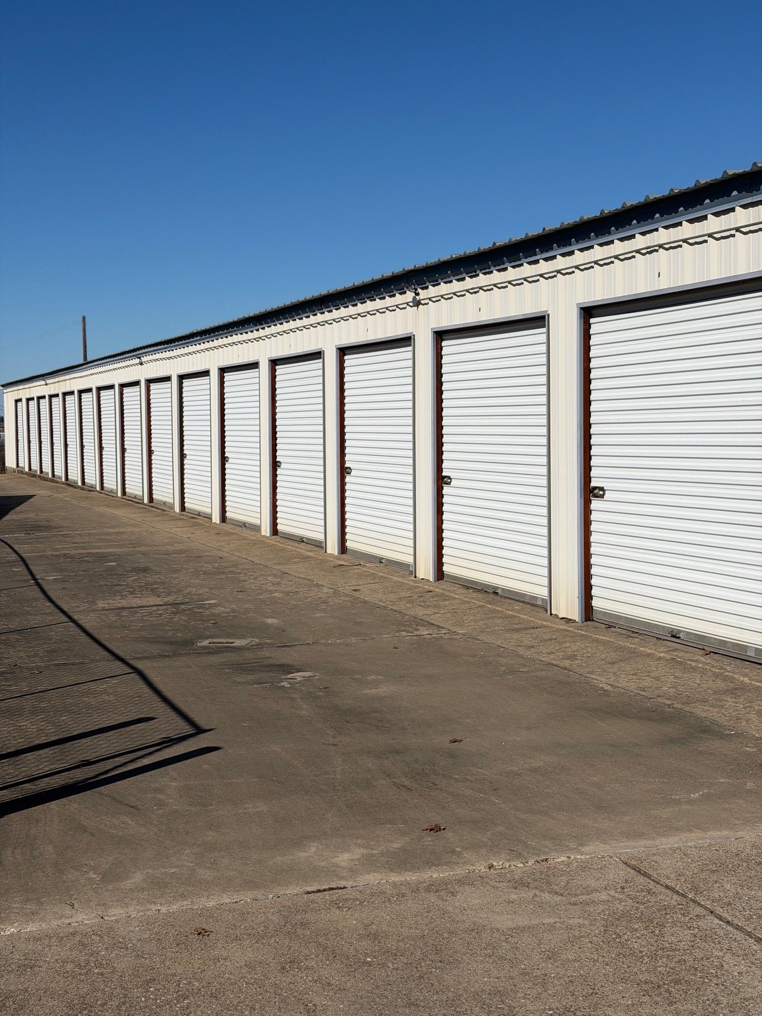 Row of white storage unit doors under a blue sky, on a paved lot.