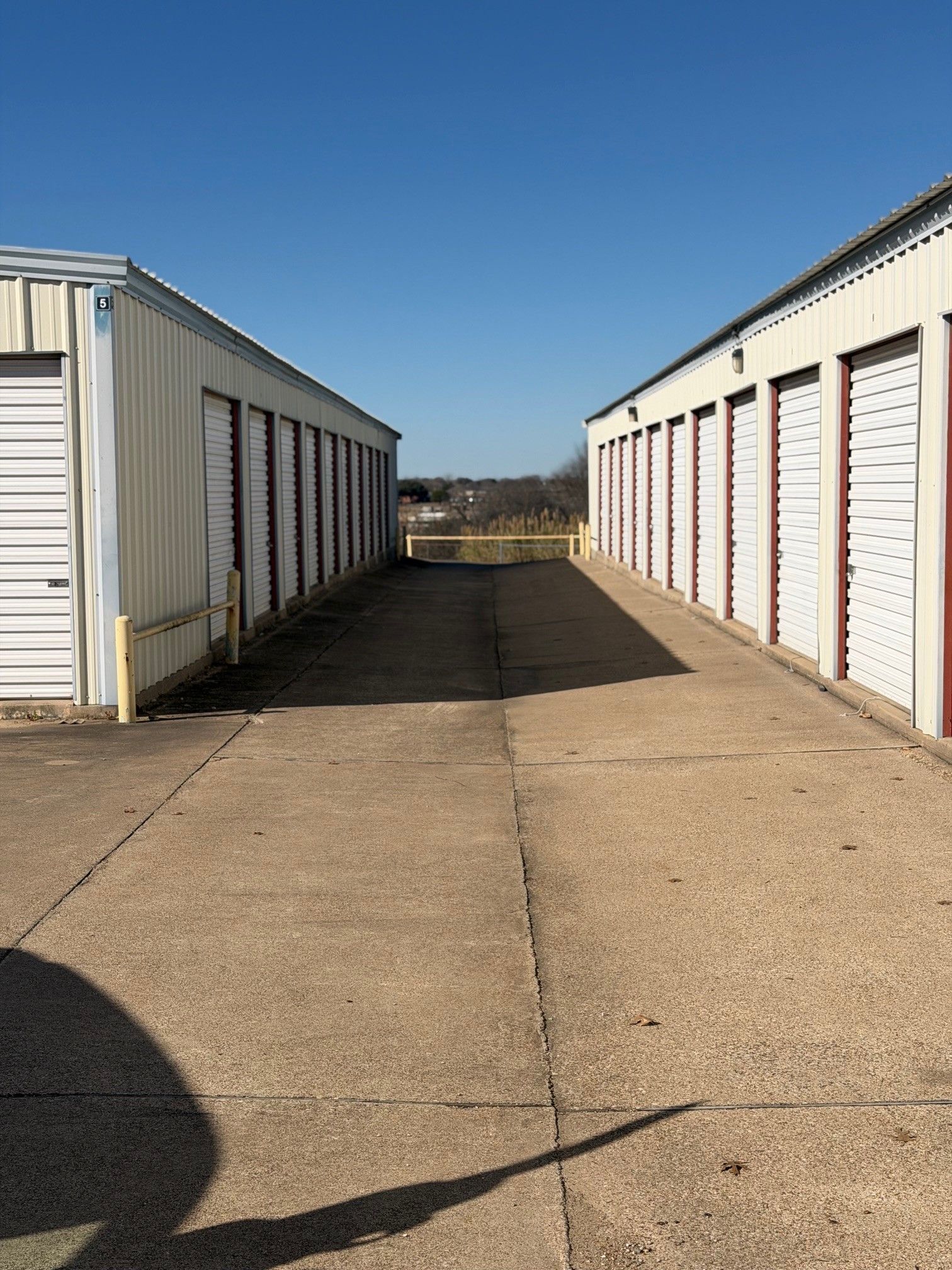 Storage units line a concrete path, under a blue sky.