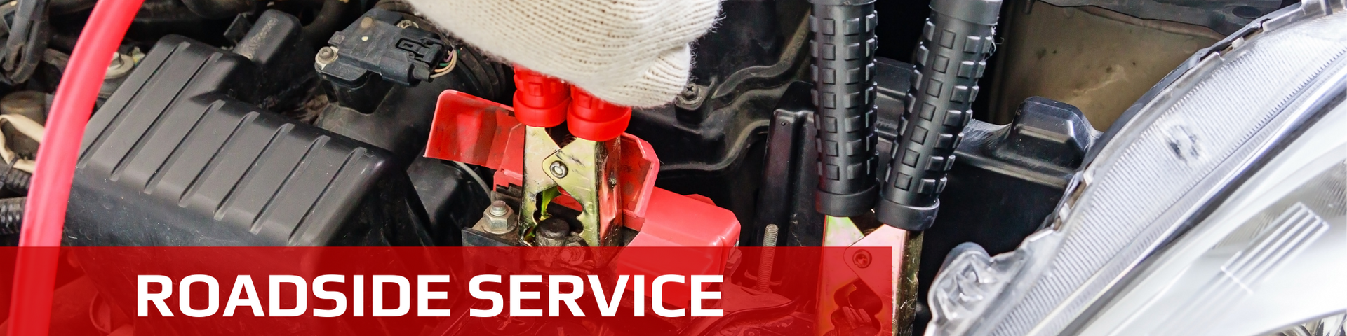 Red car battery terminal being worked on, with a roadside service label.