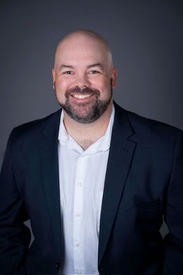 Smiling bald man in a navy blazer and white shirt against a dark studio background