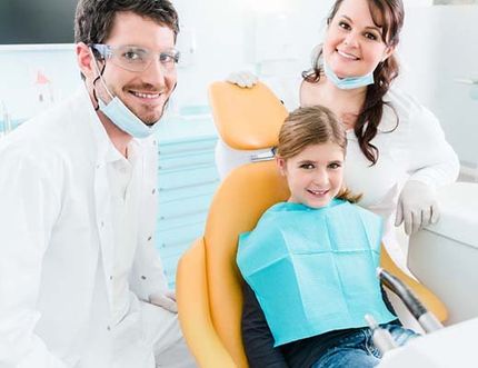 A little girl is sitting in a dental chair with her parents.