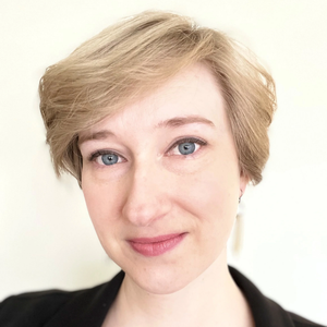 Close-up portrait of a person with short blonde hair and a slight smile against a light background
