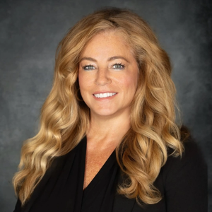 Smiling blonde woman in a black blazer against a dark studio backdrop