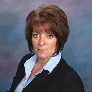 Head-and-shoulders studio portrait of a woman in a black blazer and light blue shirt on a gray backdrop
