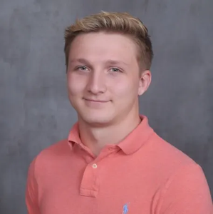 Portrait of a smiling person in a coral polo shirt against a gray studio backdrop