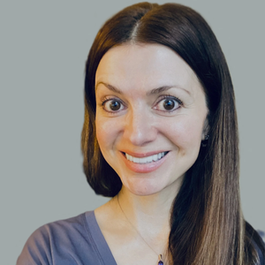 Smiling woman with long dark hair in a gray top against a plain gray background