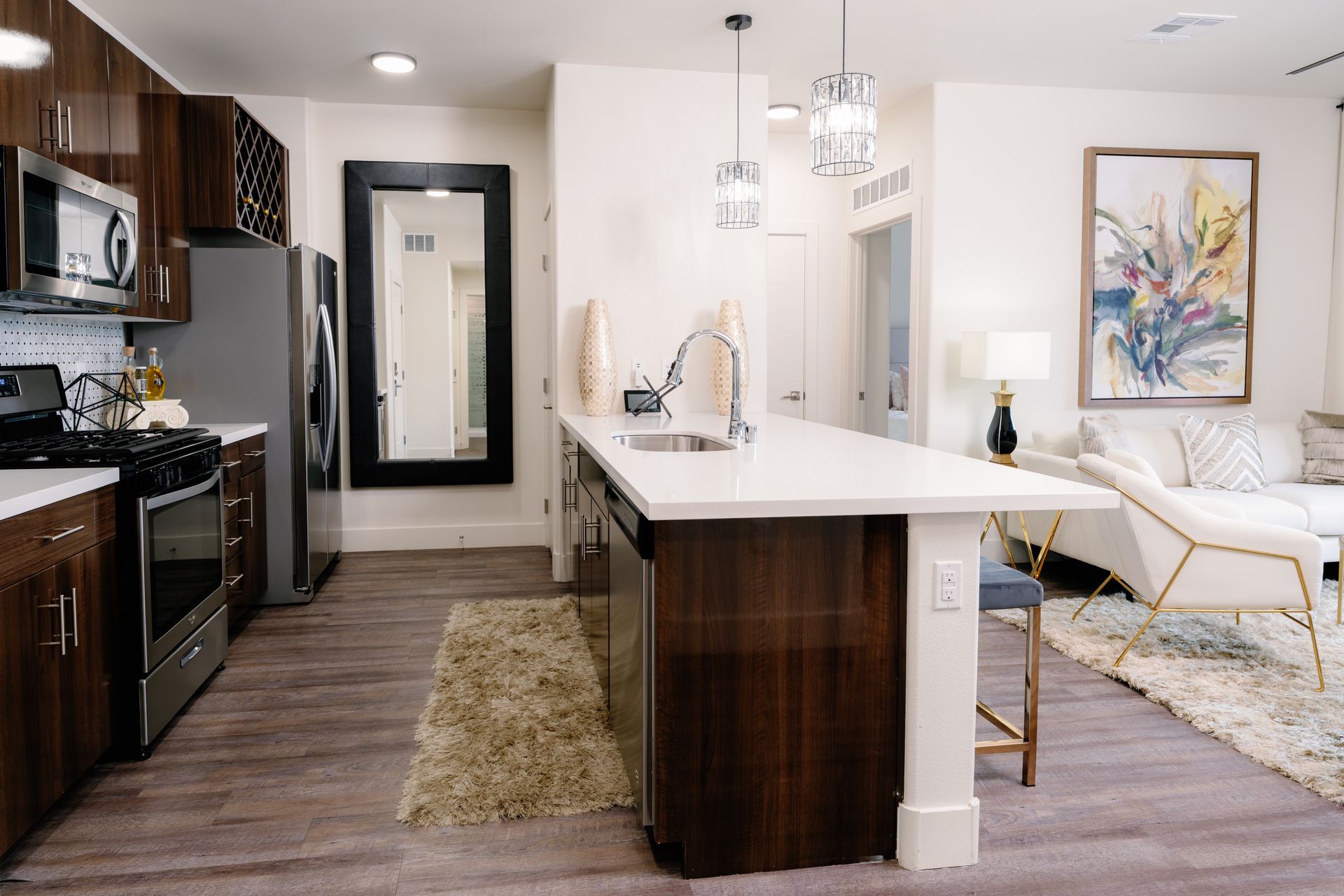 Modern open-plan kitchen and living room with island, dark cabinets, white chairs, and neutral decor.