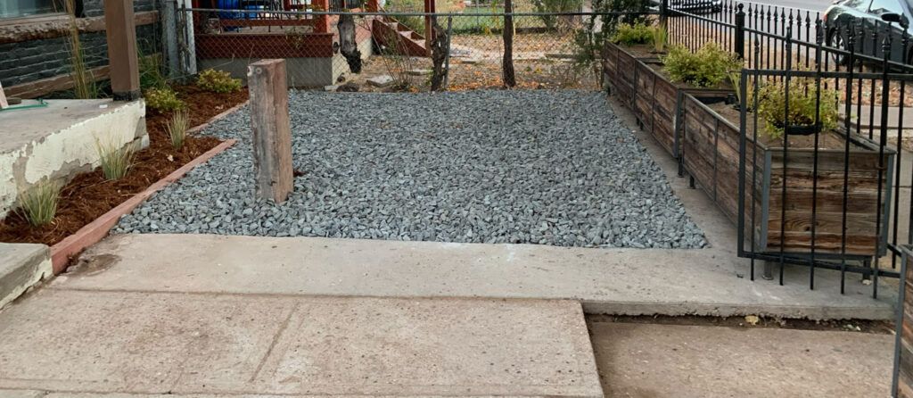 A concrete walkway leading to a gravel area with a fence in the background.