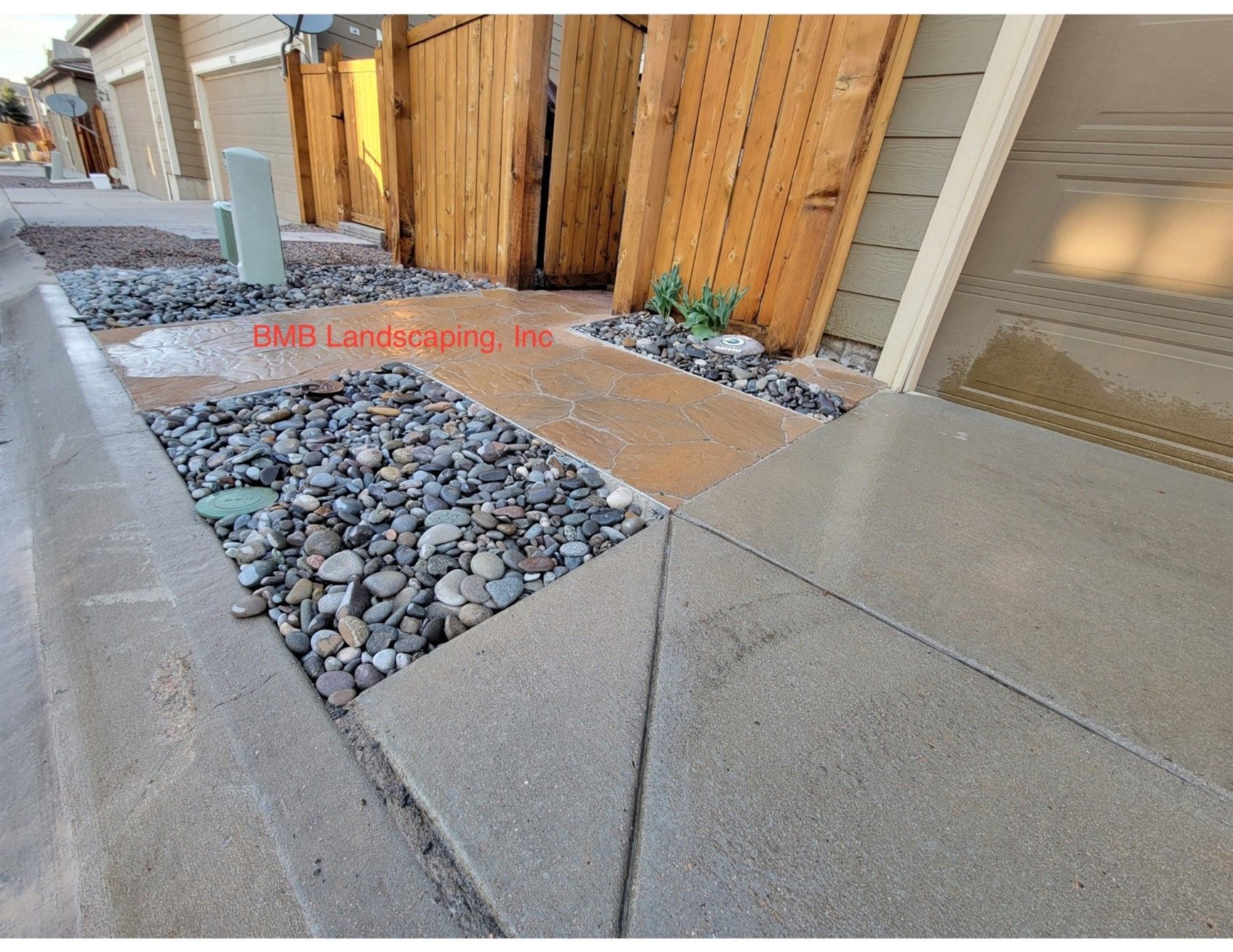 A concrete walkway with rocks and a wooden fence in front of a house.