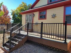 A yellow house with a black railing and stairs leading up to it.