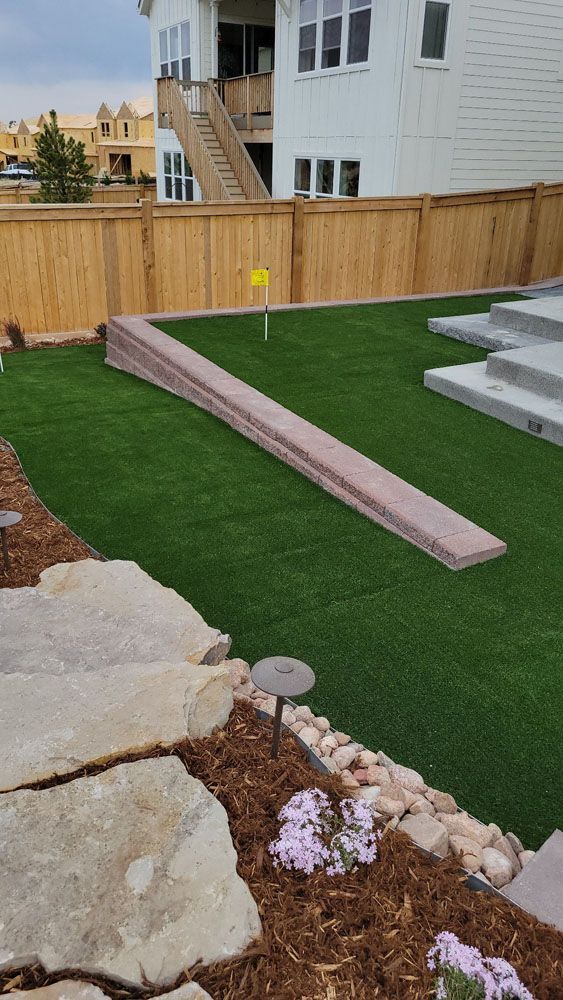 A backyard with a wooden fence , grass , rocks and flowers.