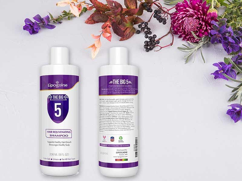 Two bottles of shampoo are sitting on a table next to flowers.