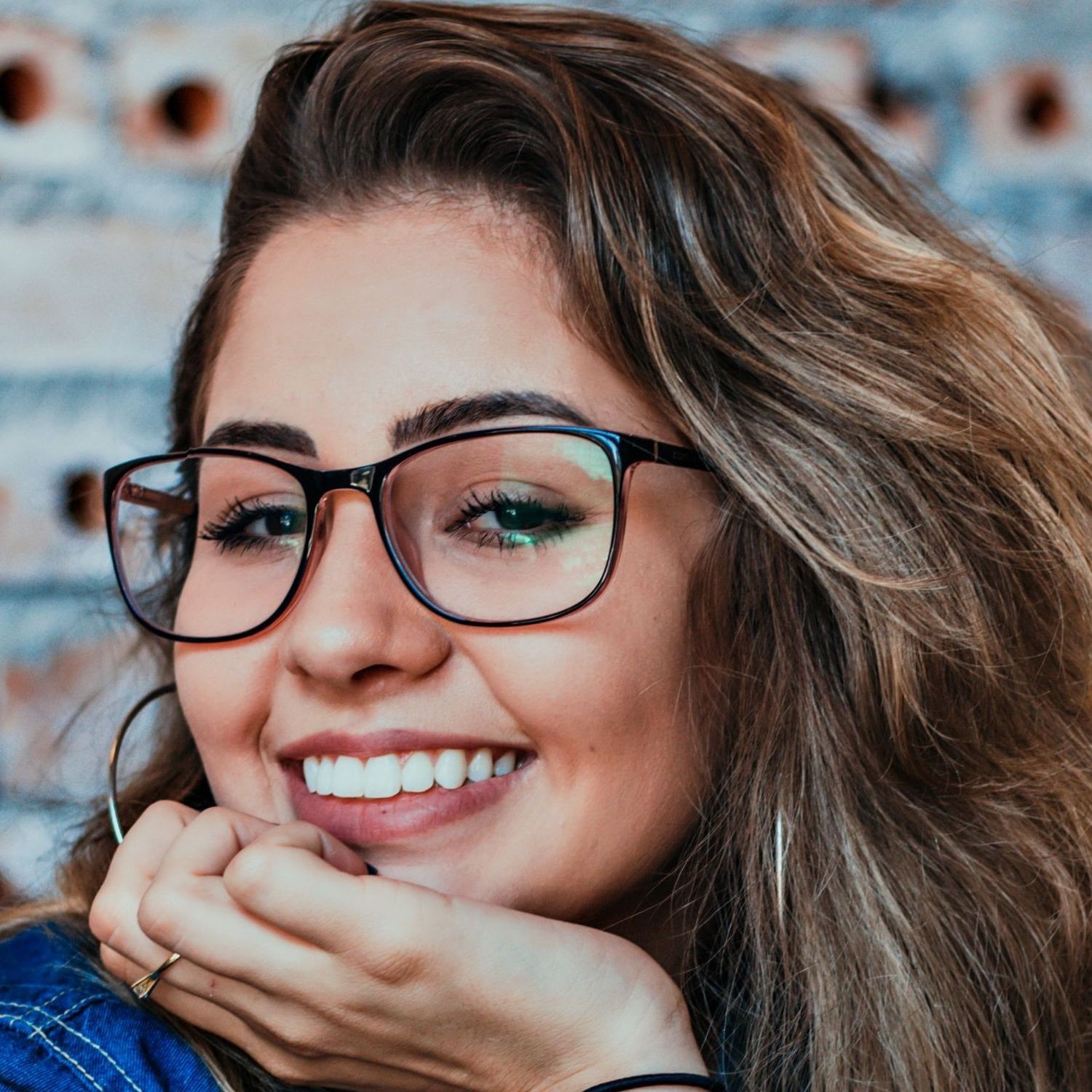 a woman wearing glasses is smiling and covering her mouth with her hand .