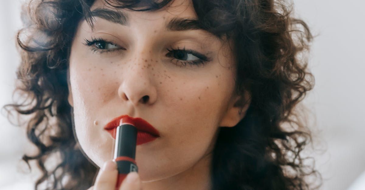 A woman with curly hair is applying red lipstick to her lips.