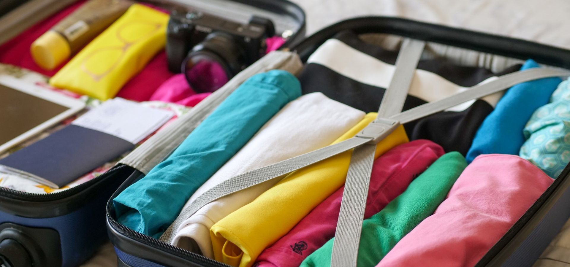 a suitcase filled with clothes and a camera on a bed .