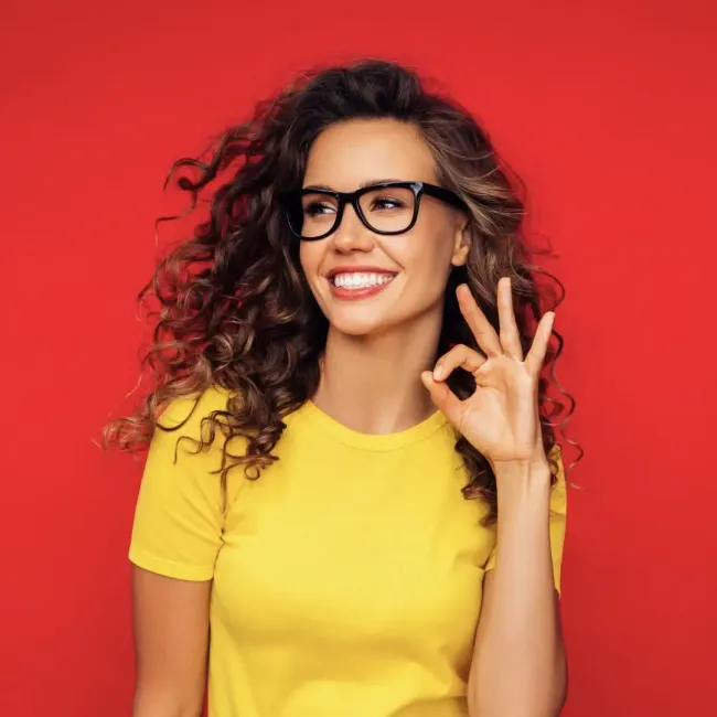 a woman wearing glasses and a yellow shirt is giving an ok sign after getting teeth whitened.