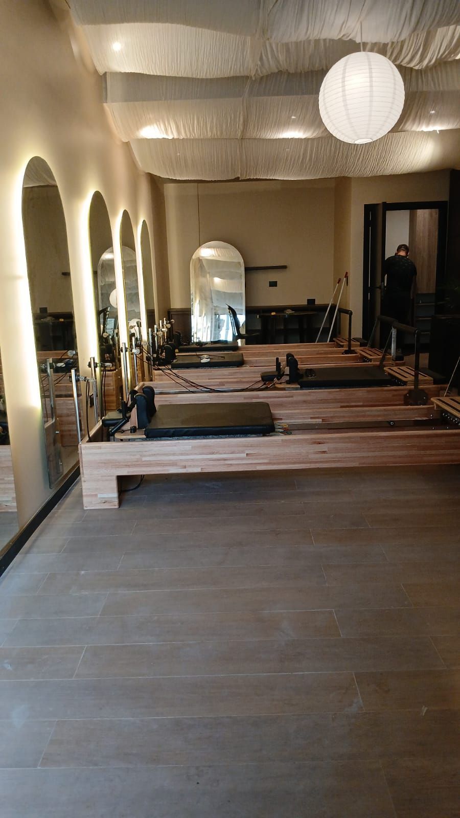 Moderno estudio de fitness con máquinas de Pilates reformer, espejos arqueados y lámparas colgantes esféricas.