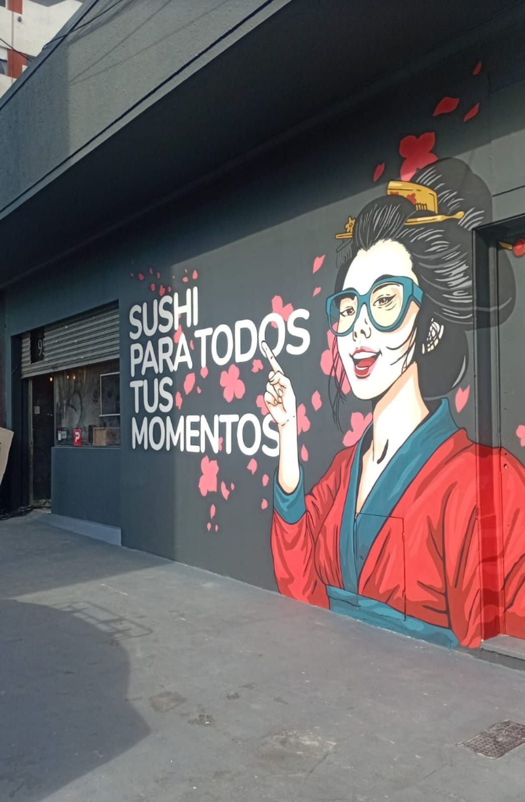 Mural de una mujer sonriente vestida de rojo con el texto “Sushi para todos tus momentos” en la pared de una tienda.