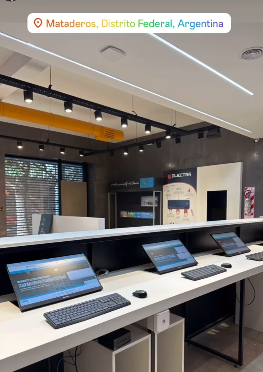 Sala de exposición moderna con mostrador blanco, ordenadores portátiles y pantallas