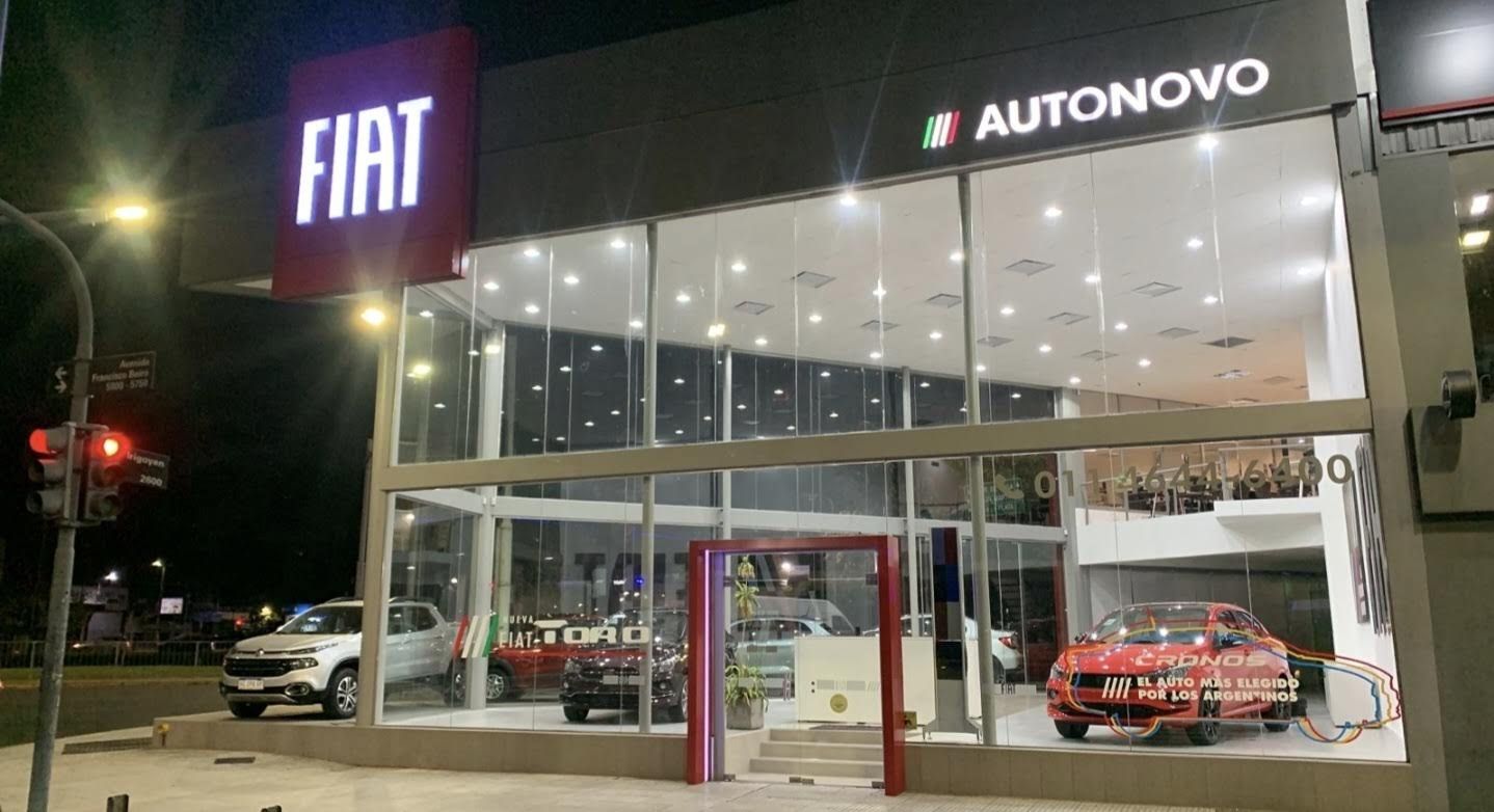 Exterior de un concesionario FIAT por la noche, con las luces brillantes de la sala de exposición y los coches expuestos.
