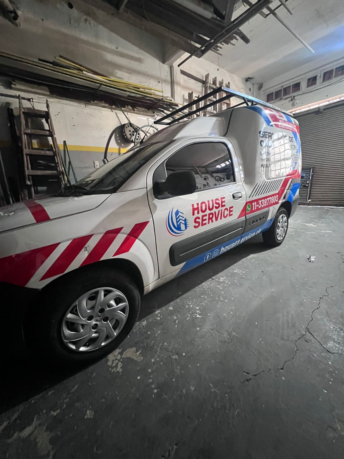Furgoneta de servicio doméstico aparcada en el interior, blanca con rayas rojas y letras azules.