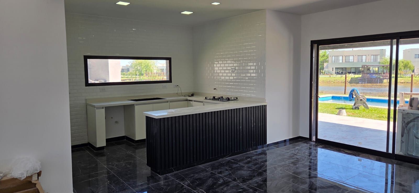 Cocina moderna con isla negra, gabinetes blancos, piso negro brillante y puertas corredizas de vidrio
