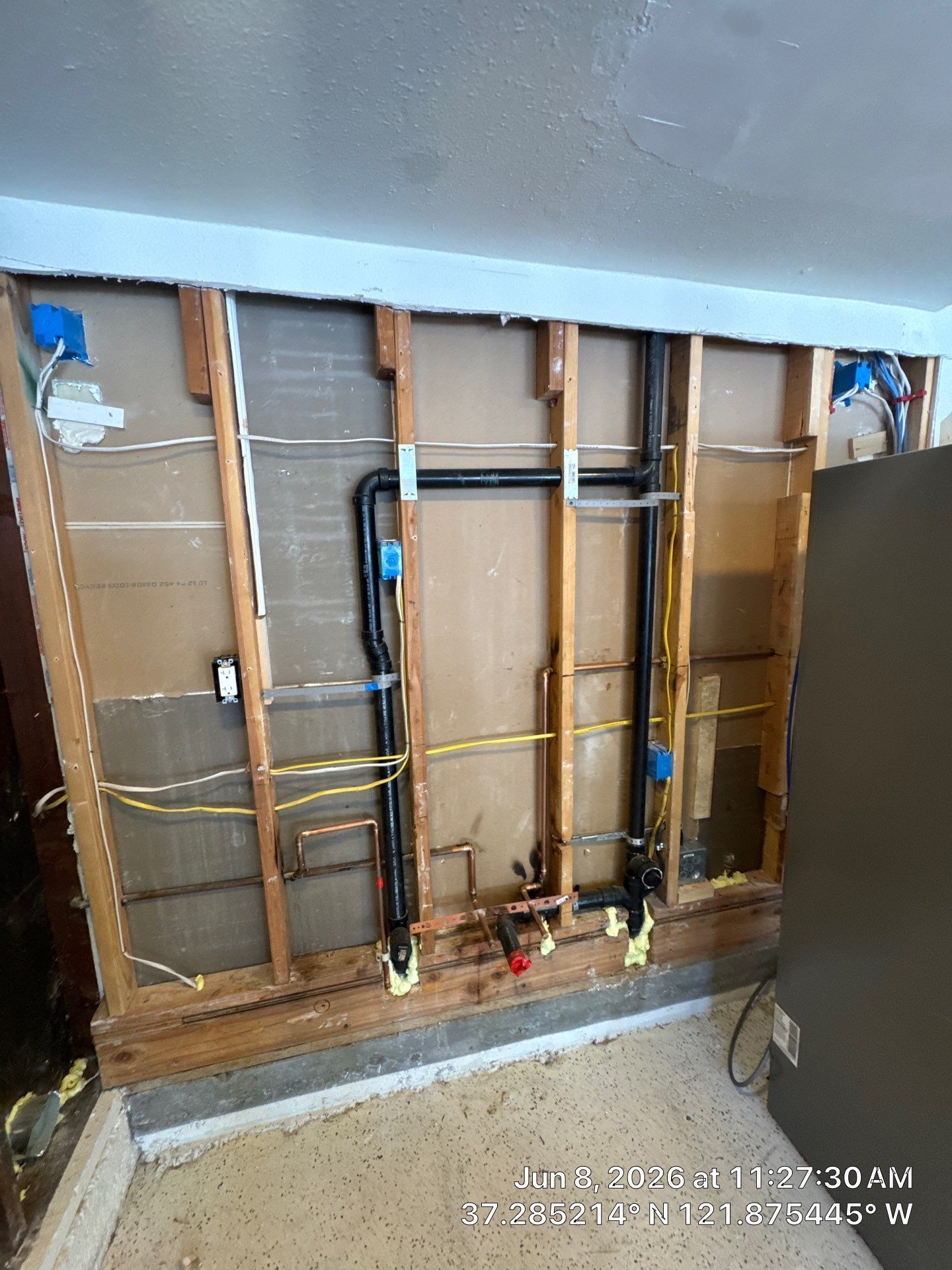 Exposed wall framing with plumbing pipes and electrical wiring during interior renovation