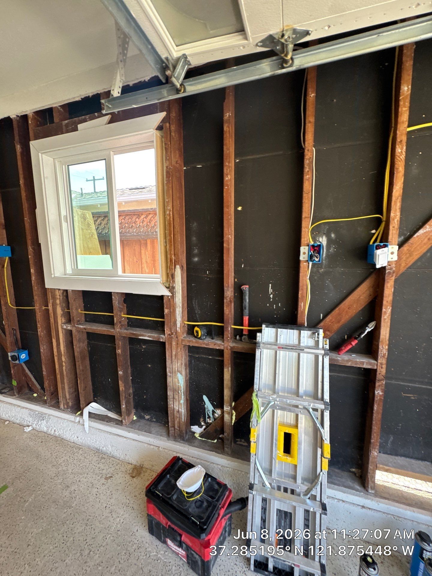 Exposed garage wall framing with a window, ladder, and tools during renovation