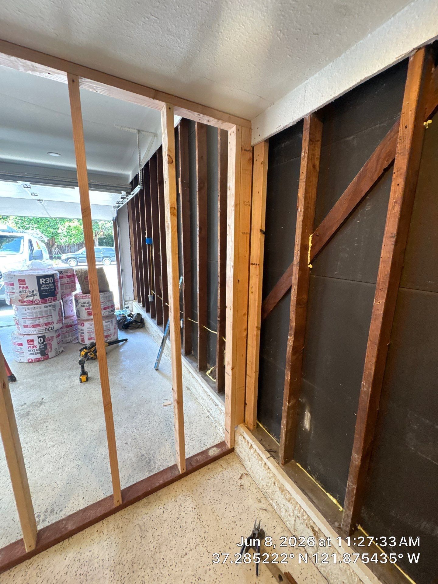 Framed interior wall under construction with exposed wooden studs and a narrow hallway leading outside