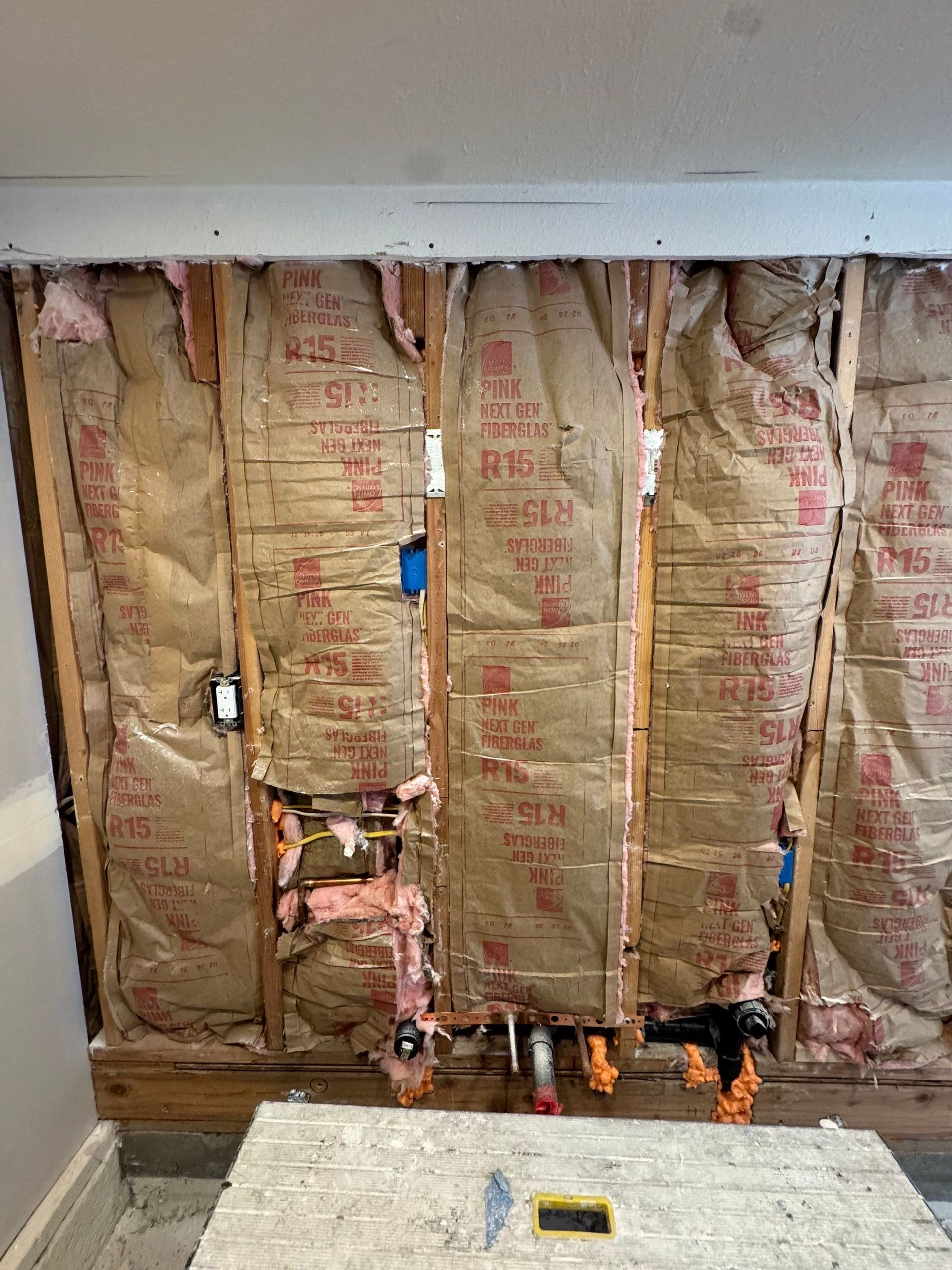 Insulation exposed in unfinished wall with plumbing and wiring behind it