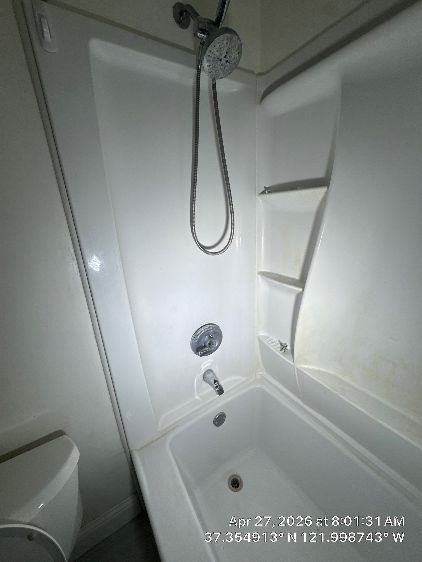 Compact white bathroom with shower, bathtub, wall shelf, and handheld showerhead