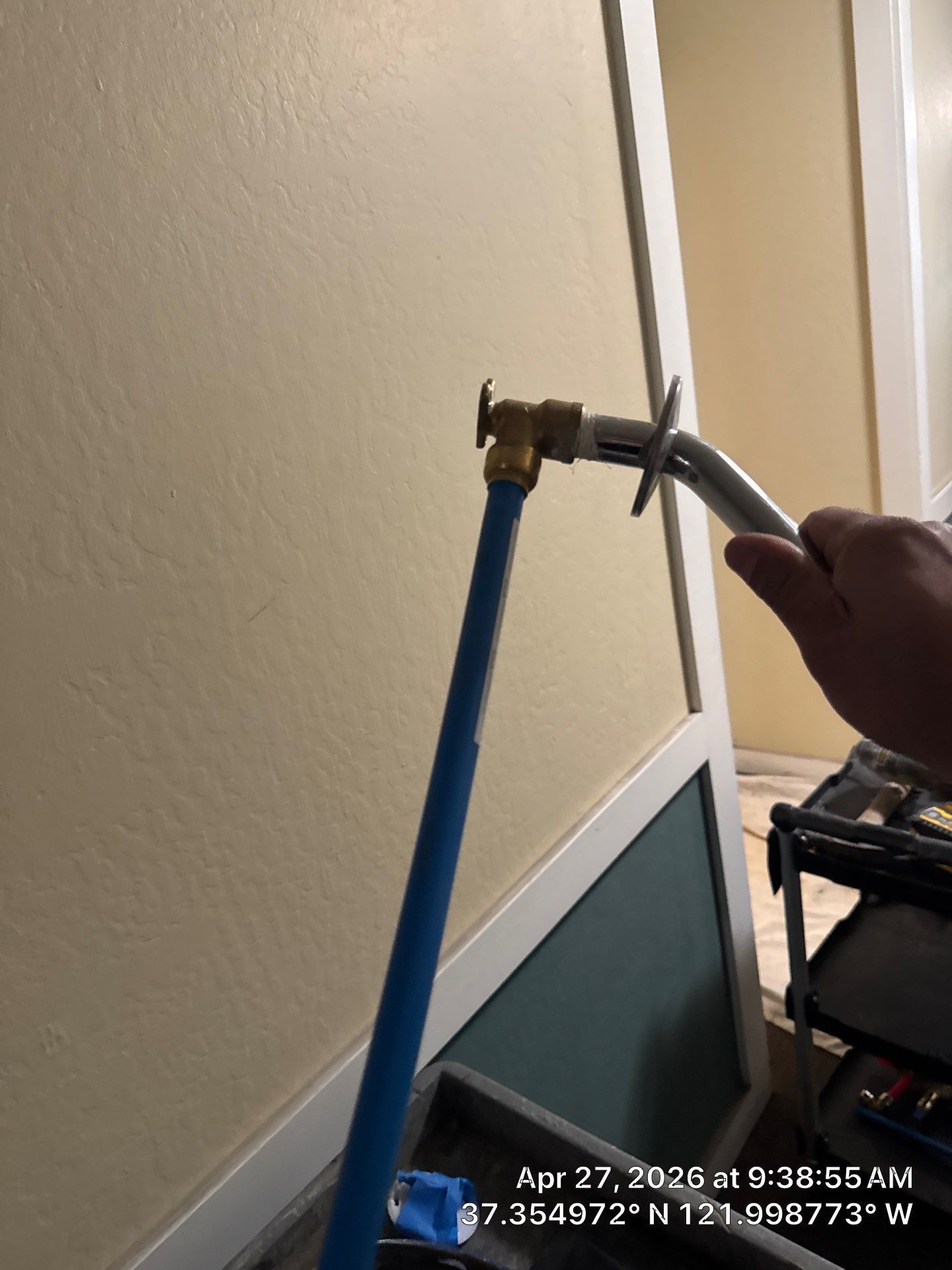 Hand holding pliers tightening a brass fitting on a blue pipe against an indoor wall.