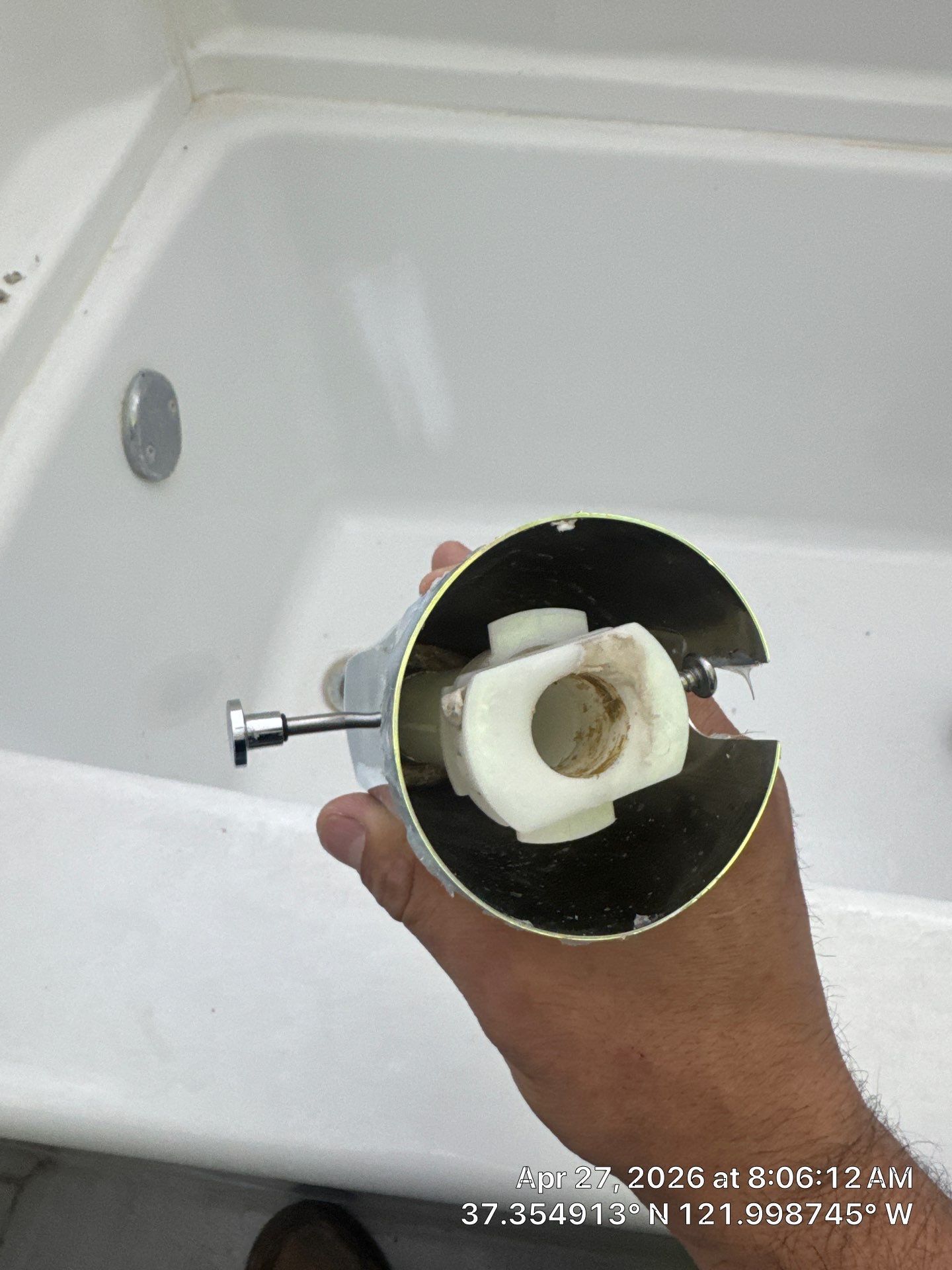 Hand holding a faucet cartridge over a white bathtub, showing the removed plumbing part.