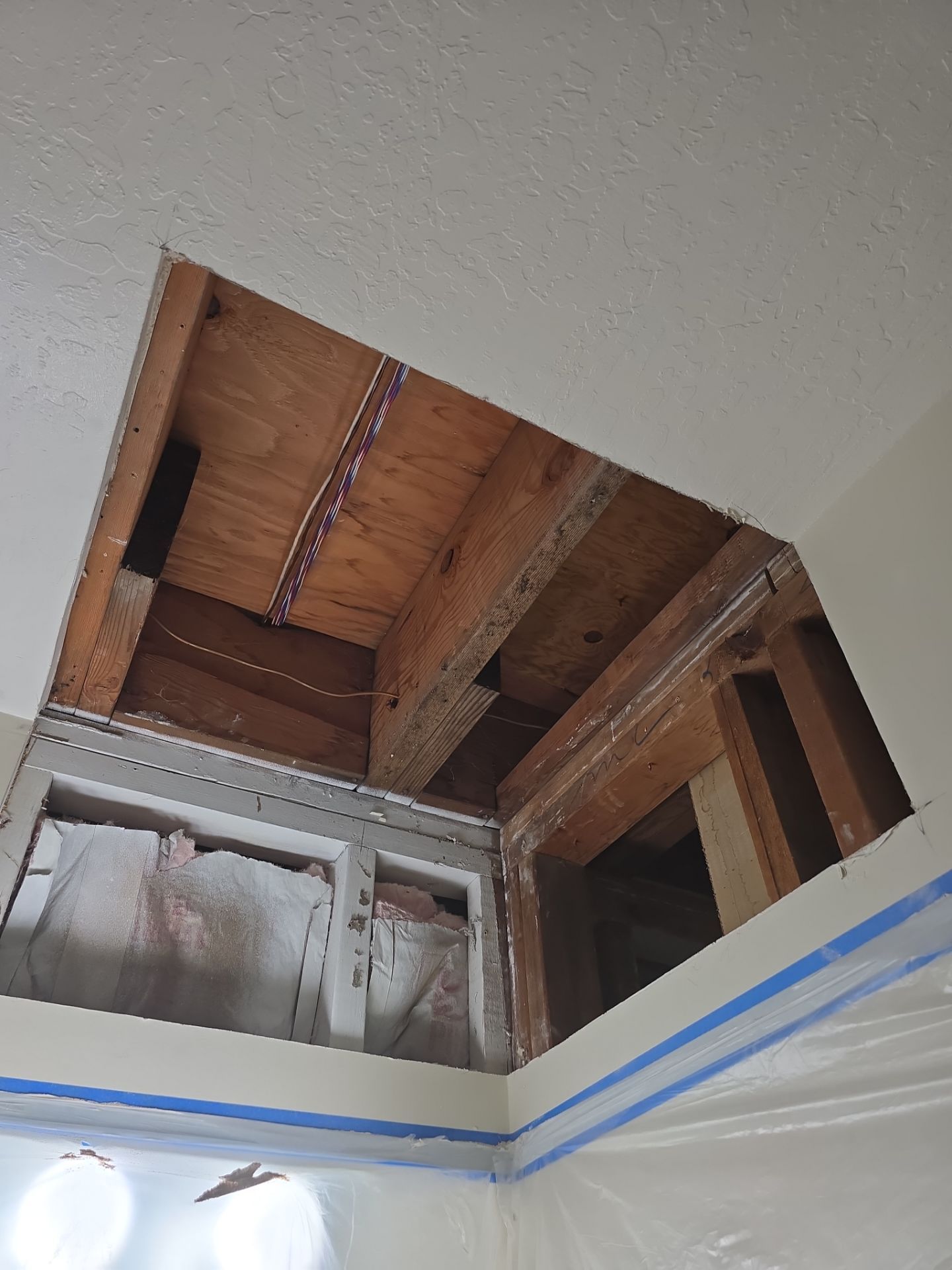Bathroom ceiling opened up exposing wooden rafters and insulation above a tiled wall.