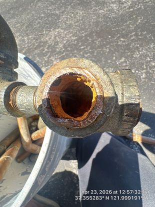 Close-up of a rusted metal pipe opening on a hose reel outdoors.
