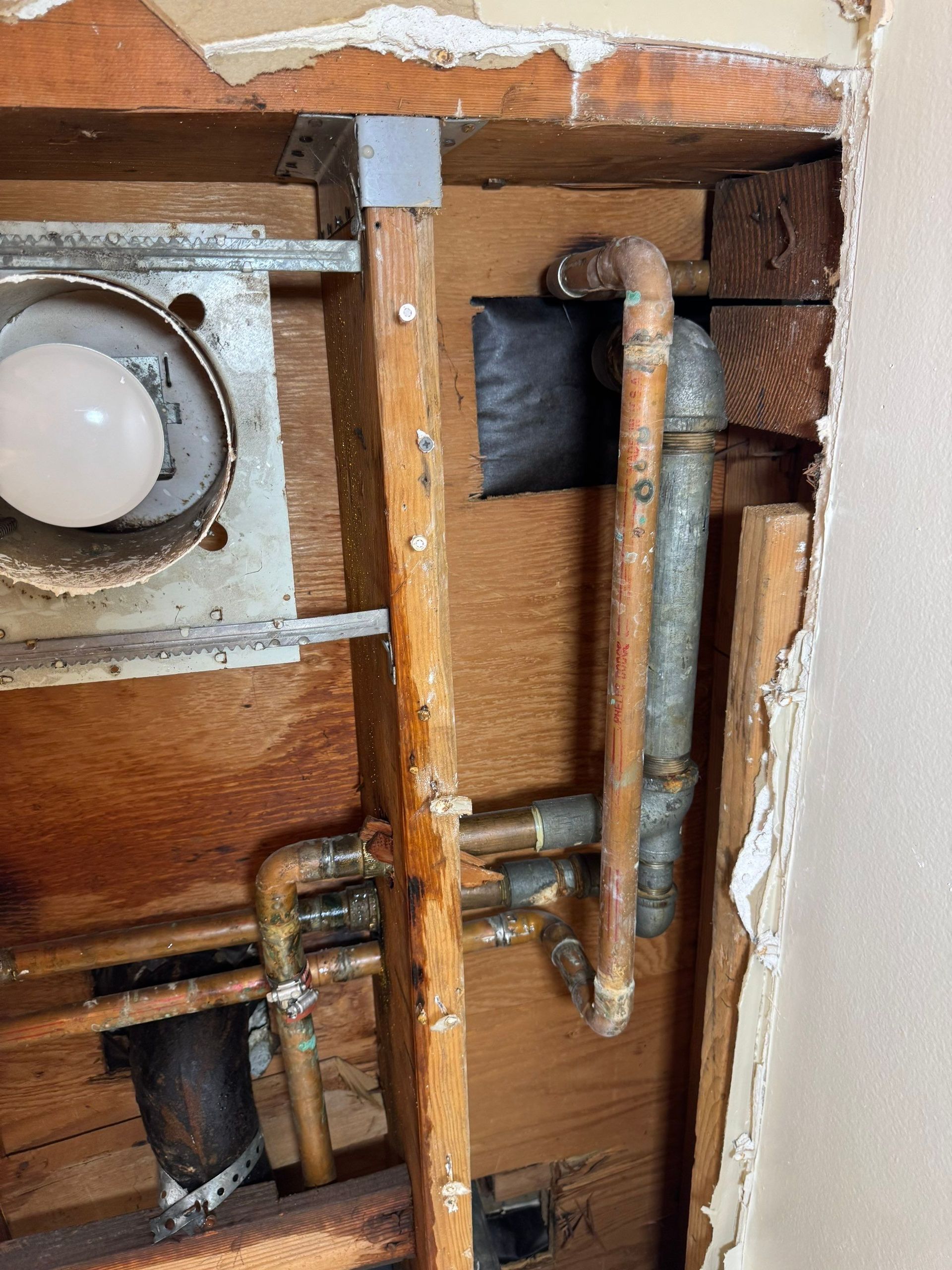 Open wall with copper pipes, valves, and a round white fixture inside a wooden cavity