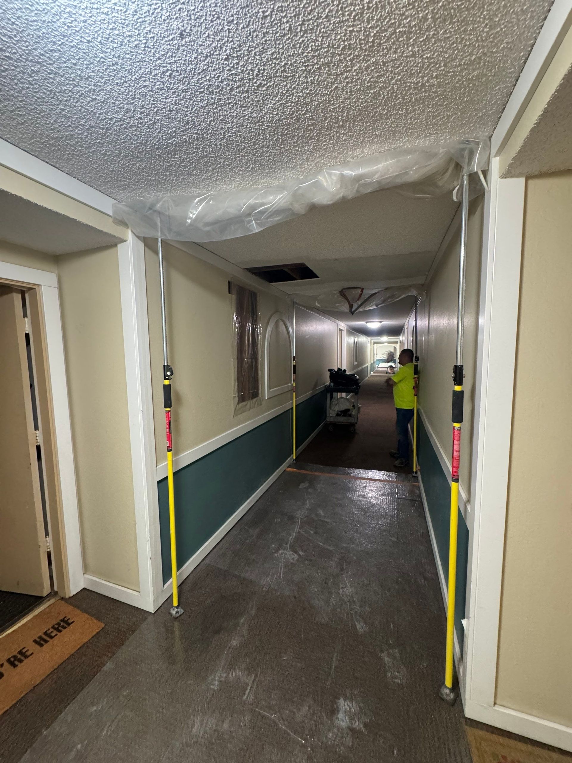 Hazy hallway with damaged ceiling; workers in yellow vests near a cart and debris.