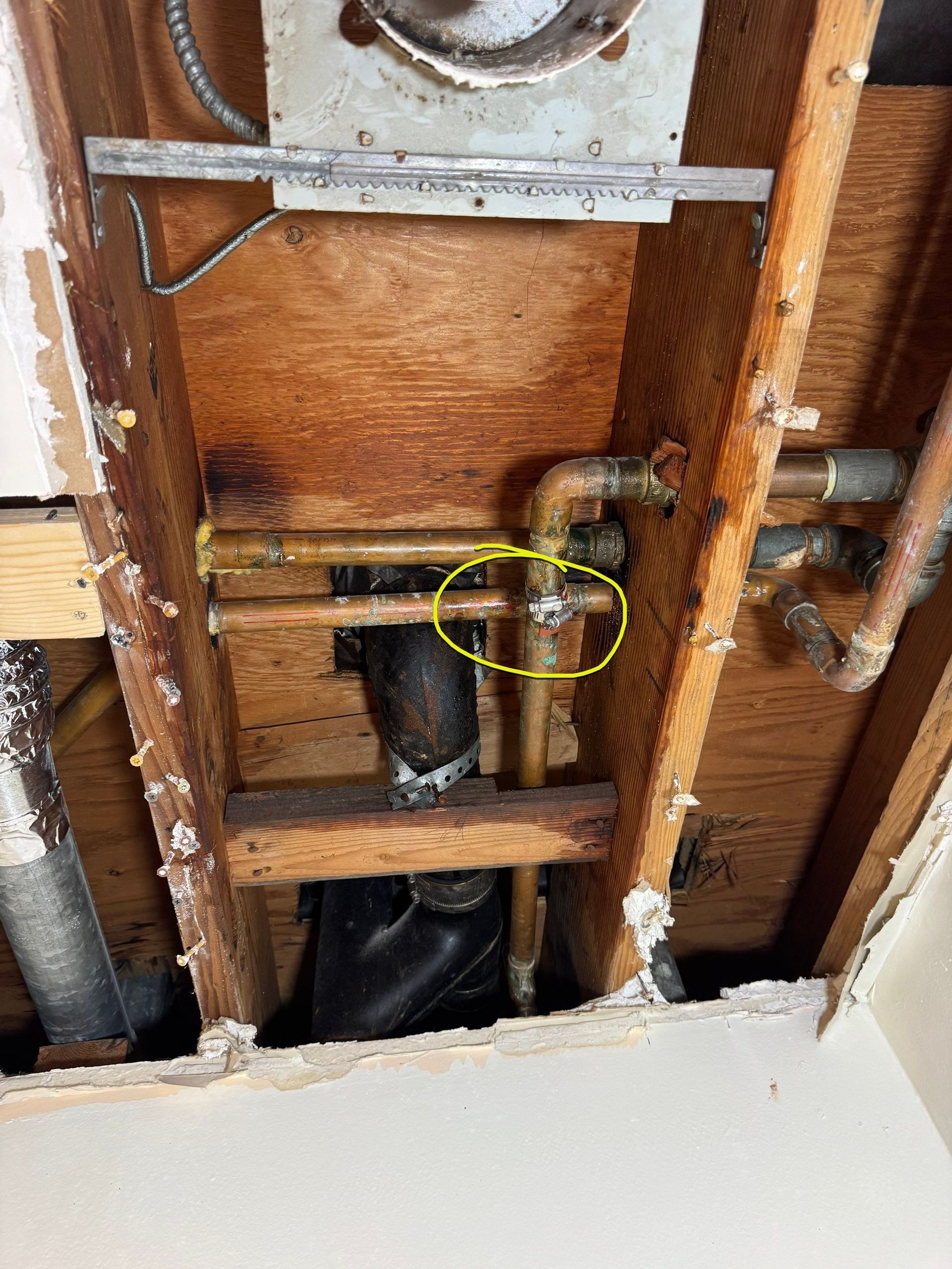Exposed plumbing and wood framing beneath a sink, with a yellow-circled pipe joint.