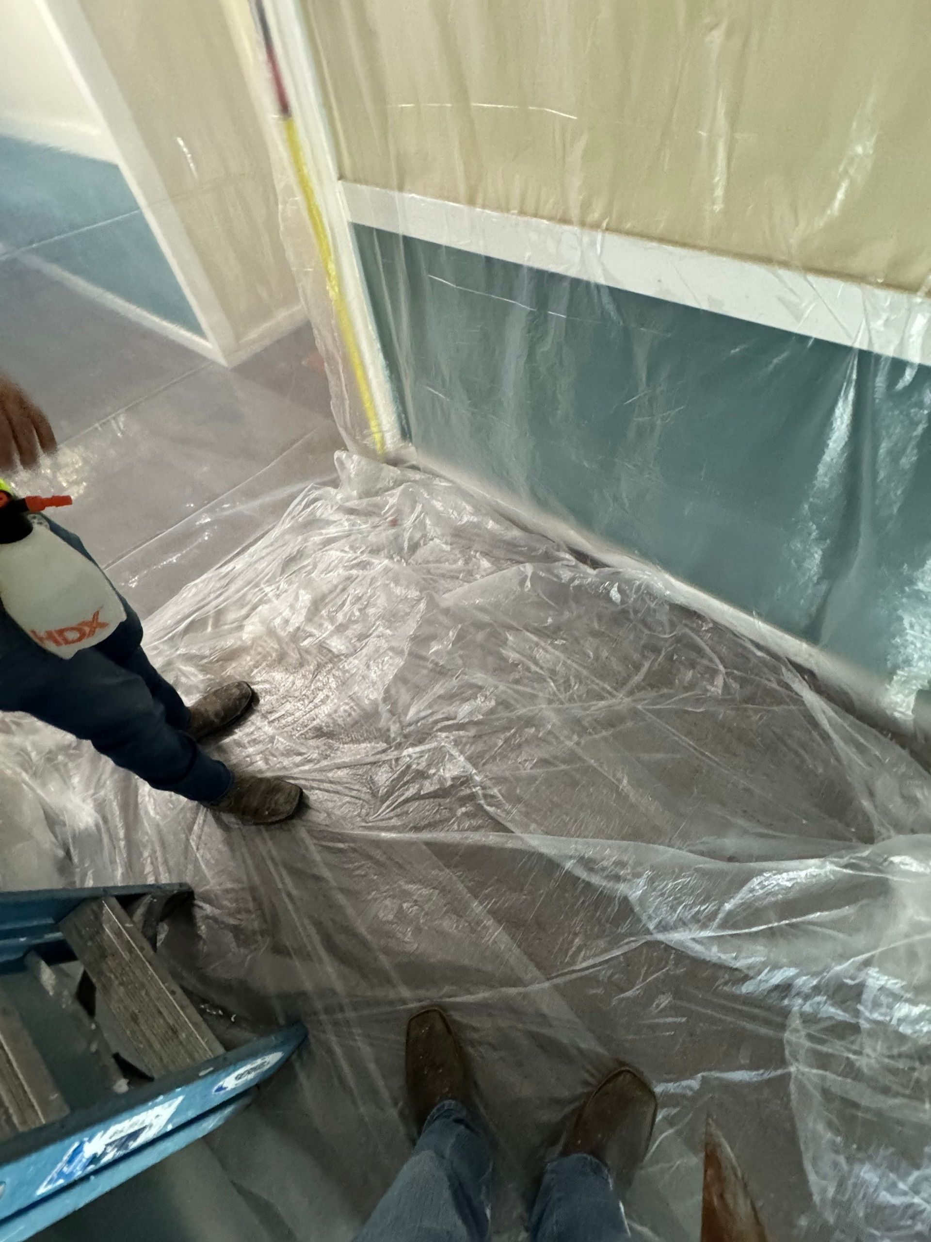 People standing in a room covered with plastic sheeting and tape, as if for painting or renovation.