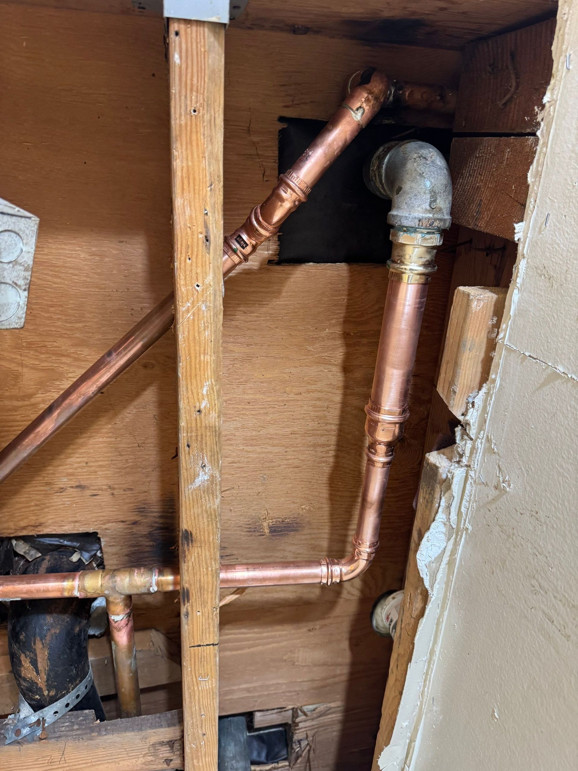 Copper plumbing pipes inside a wall cavity, including a vertical pipe with an elbow joint.