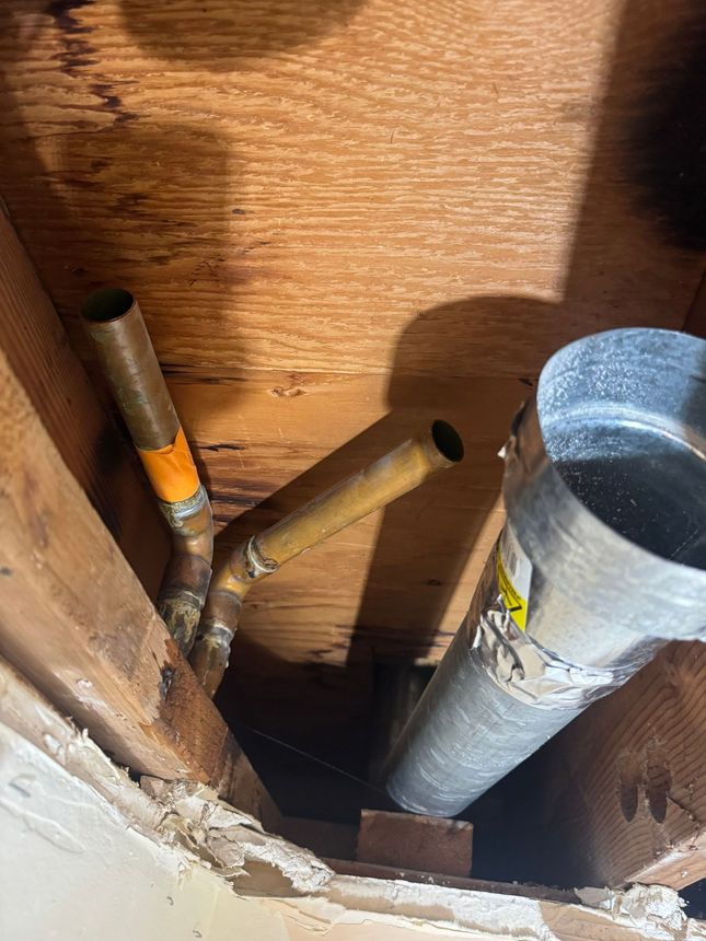 Exposed copper pipes and a galvanized vent pipe inside a wooden wall cavity during construction