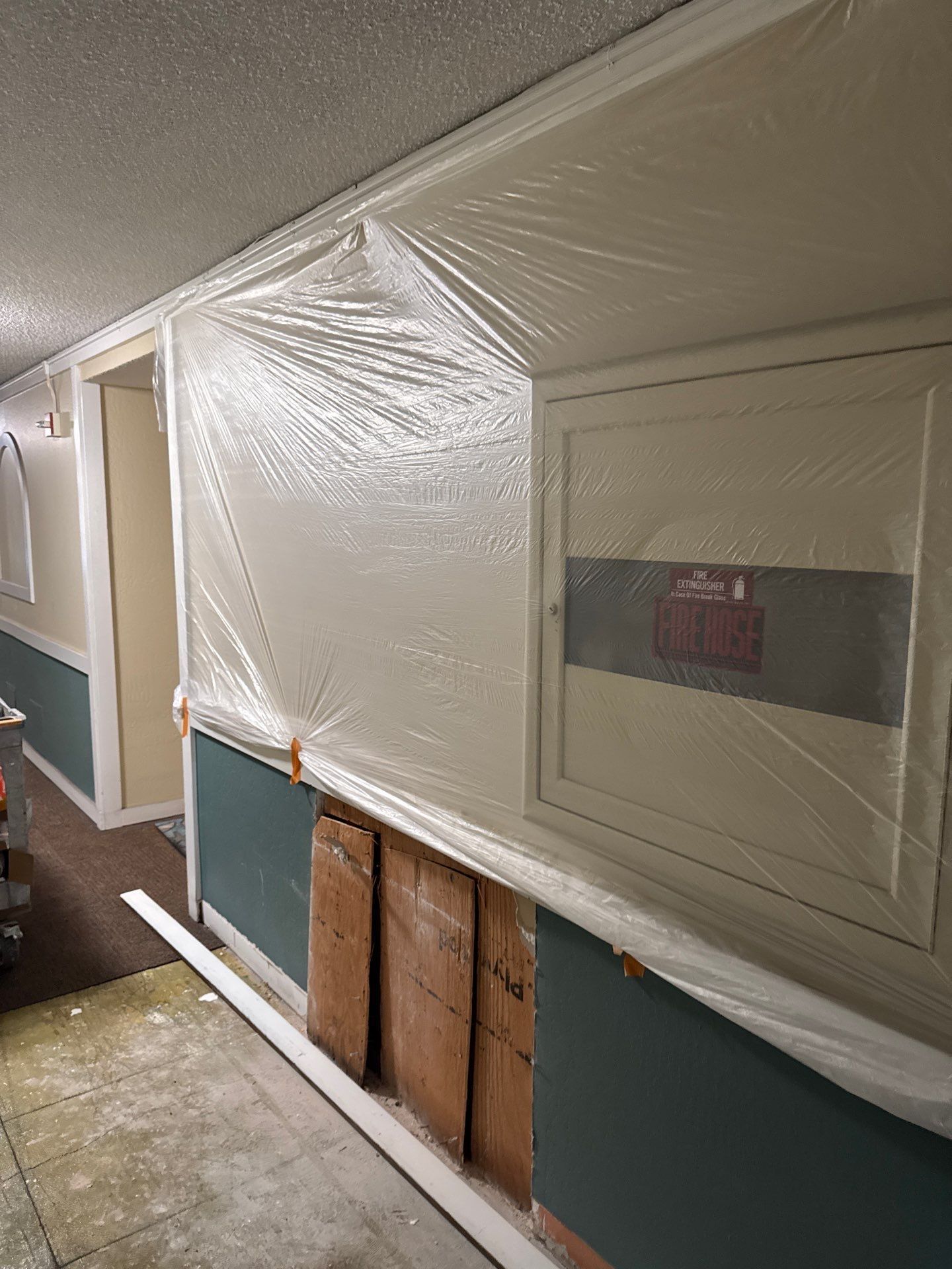 Hallway wall covered in plastic sheeting, with exposed studs and a window covered in tape.