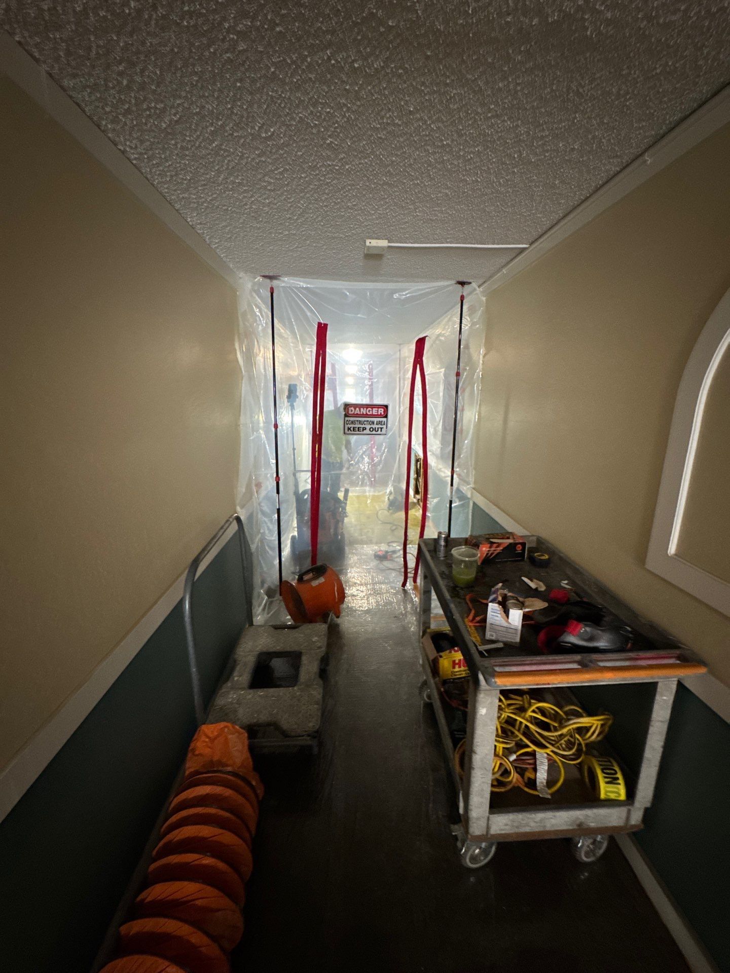 Narrow utility hallway with cleaning tools, a cart, and supplies lined along both sides