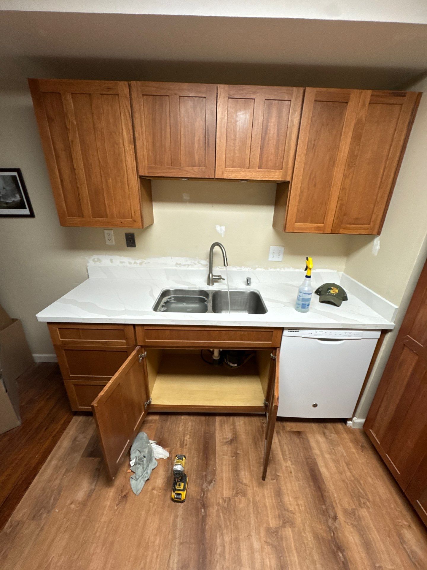 Compact kitchen with wood cabinets, white countertop, sink, mini fridge, and open lower cabinet storage.