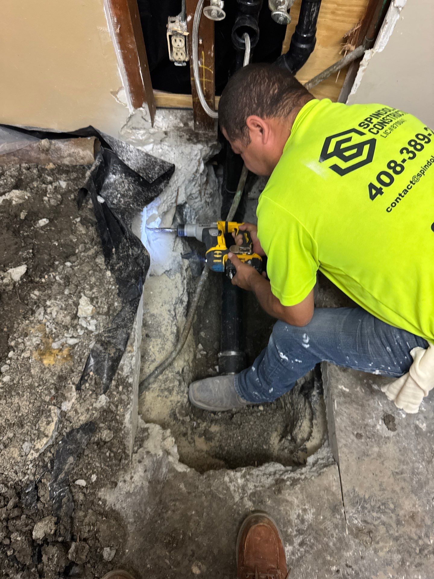 Technician in neon shirt using a drill to repair a broken pipe in a floor opening