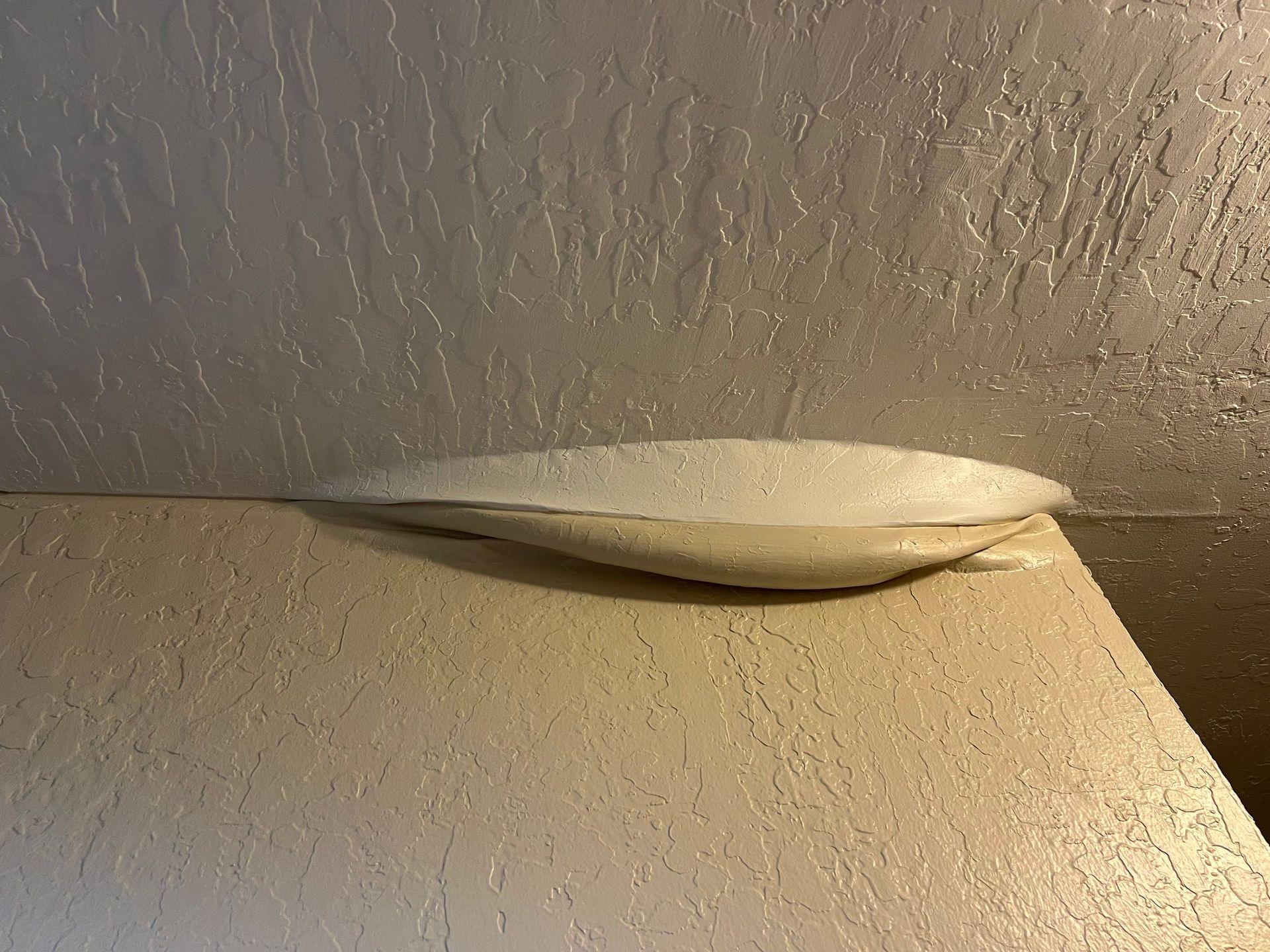 White wall-mounted light fixture with a broken or sagging cover near the ceiling corner