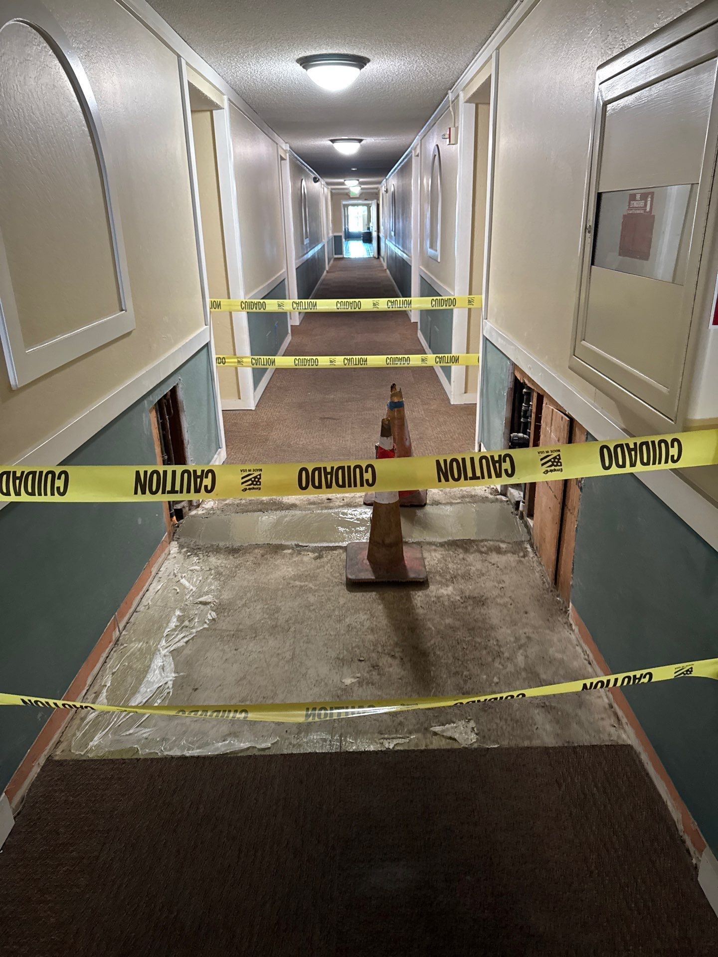 Apartment hallway blocked by caution tape and a wet floor sign, with torn flooring exposed.