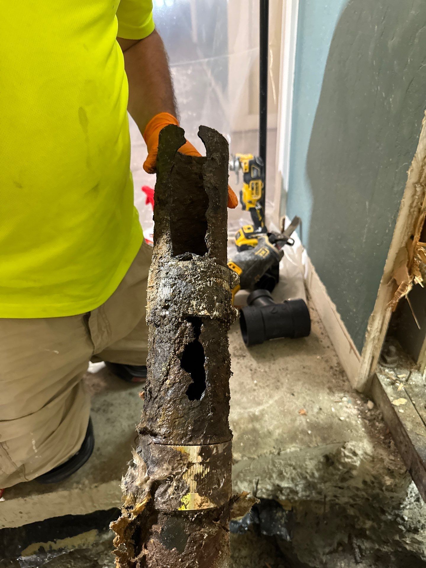 Corroded metal pipe standing upright in a construction area, with a worker in a neon shirt nearby